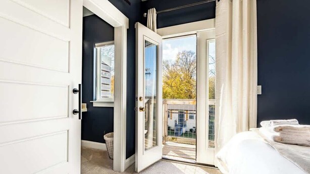 A bedroom with a large bed, a window with a view of trees, and a door leading to an outdoor area.