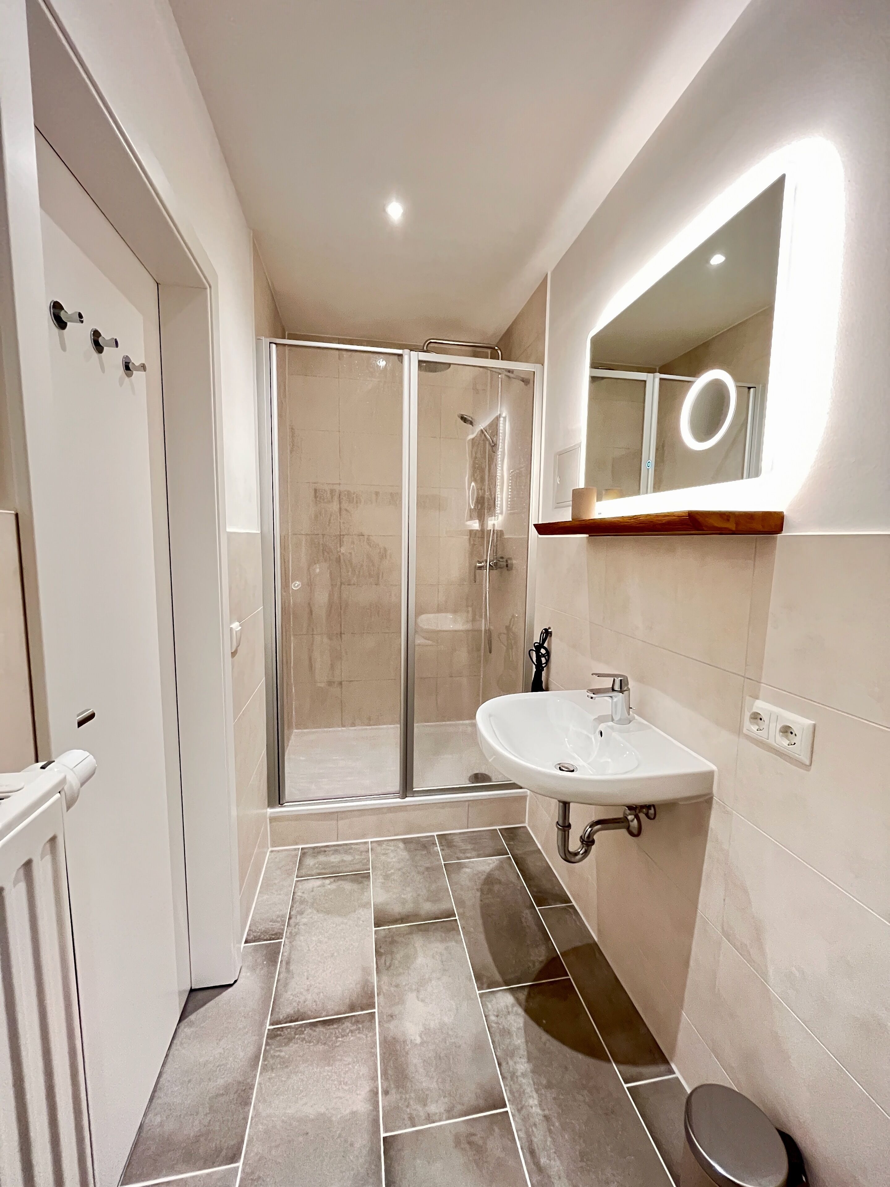 Une salle de bain moderne avec une douche à parois de verre, un lavabo blanc et un miroir doté d'un anneau lumineux.