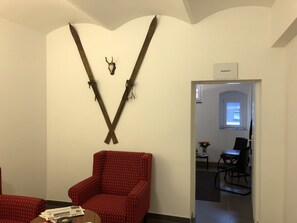 A reception area with a V-shaped wooden decoration, a red patterned chair, and a table with a newspaper and a book.