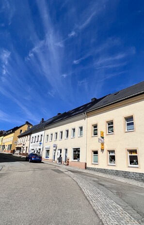 A street view with buildings, a parked car, and a clear blue sky.