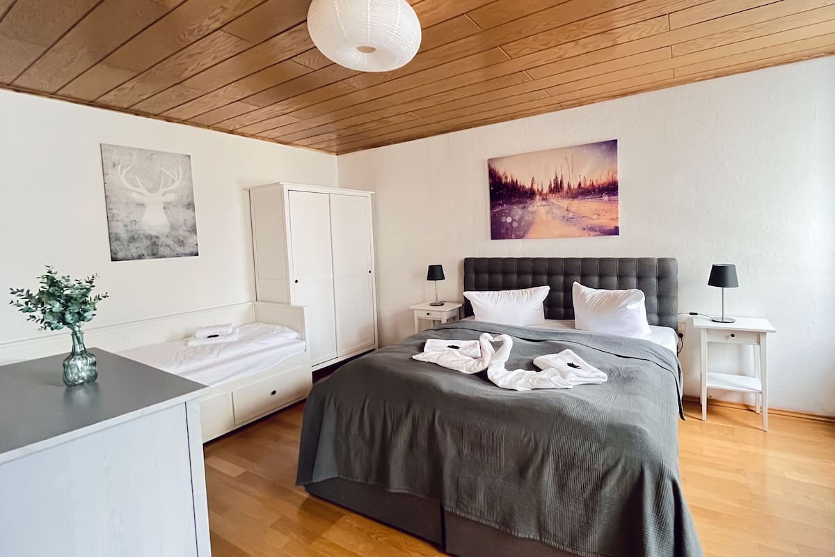 Quarto com cama, mesas de cabeceira, guarda-roupa, um quadro e uma luminária no teto.
