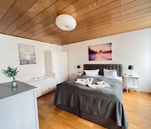 A bedroom with a bed, bedside tables, a wardrobe, a painting, and a ceiling light.