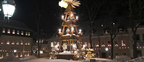 Un espace extérieur enneigé, agrémenté d’une structure décorative à plusieurs niveaux et illuminée, entouré de bâtiments dont les fenêtres sont éclairées.