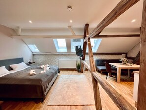 A modern loft bedroom with a sloped ceiling, skylights, a bed, a desk, and a chair.