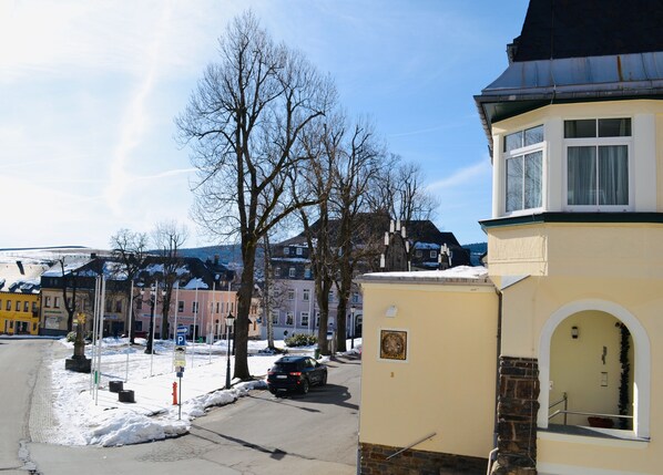 A building with a stone base and a yellow upper section, a black car parked in front, and snow on the ground.