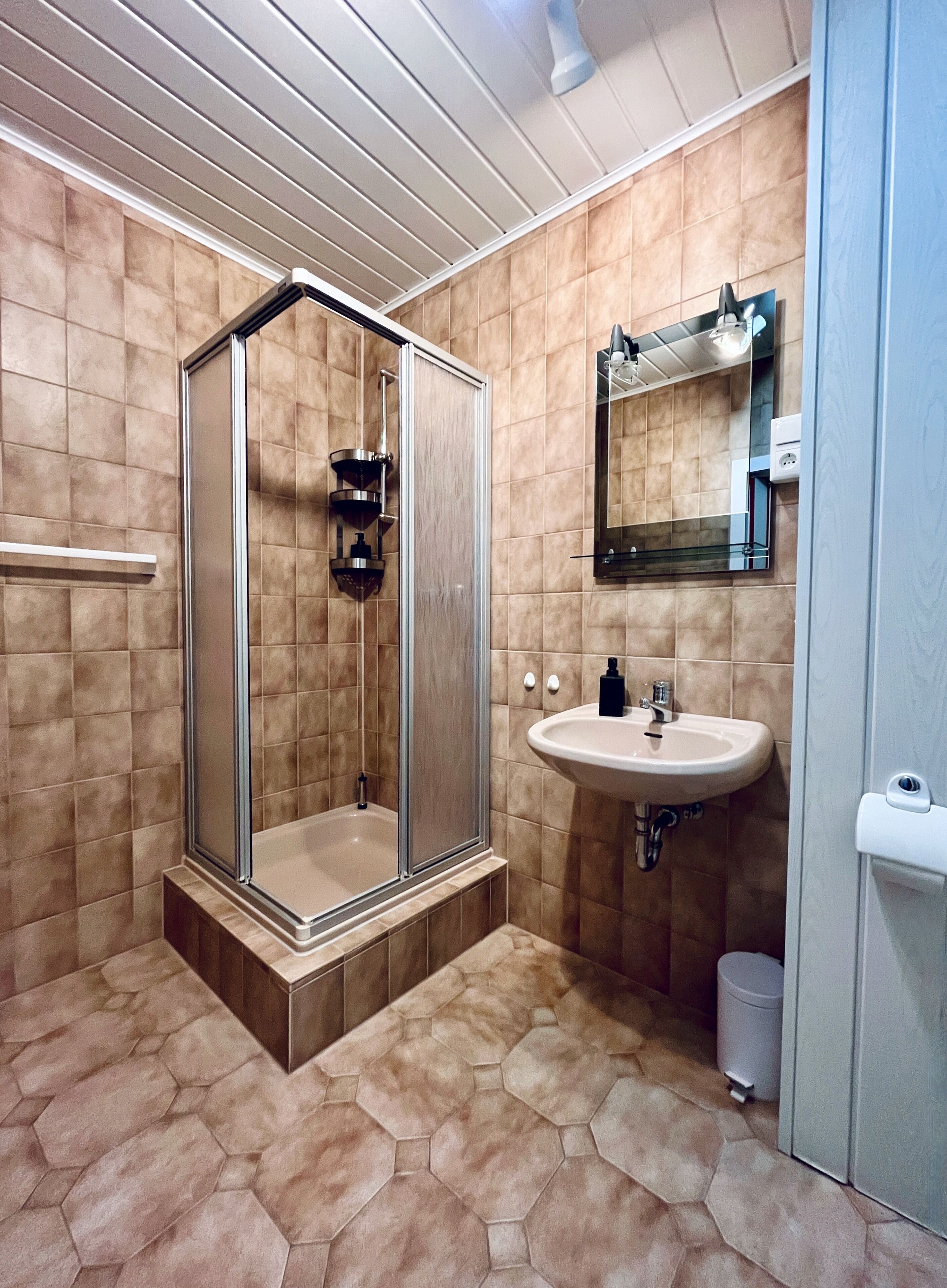 Un bagno con doccia vetro, lavandino e specchio.