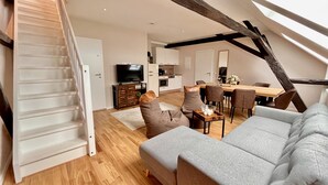 Un loft moderno con escalera, una sala de estar con sofá y sillones, un comedor con mesa y sillas, y una cocina al fondo.