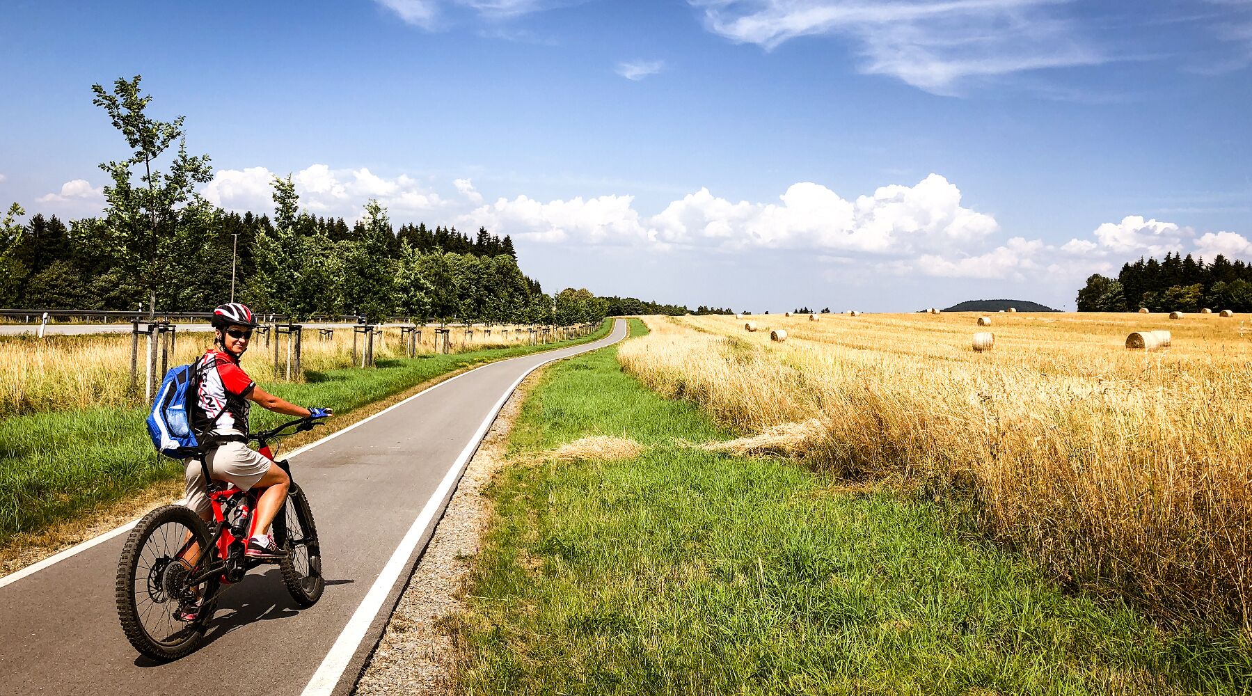 A cyclist on a paved path beside a field with hay bales.
