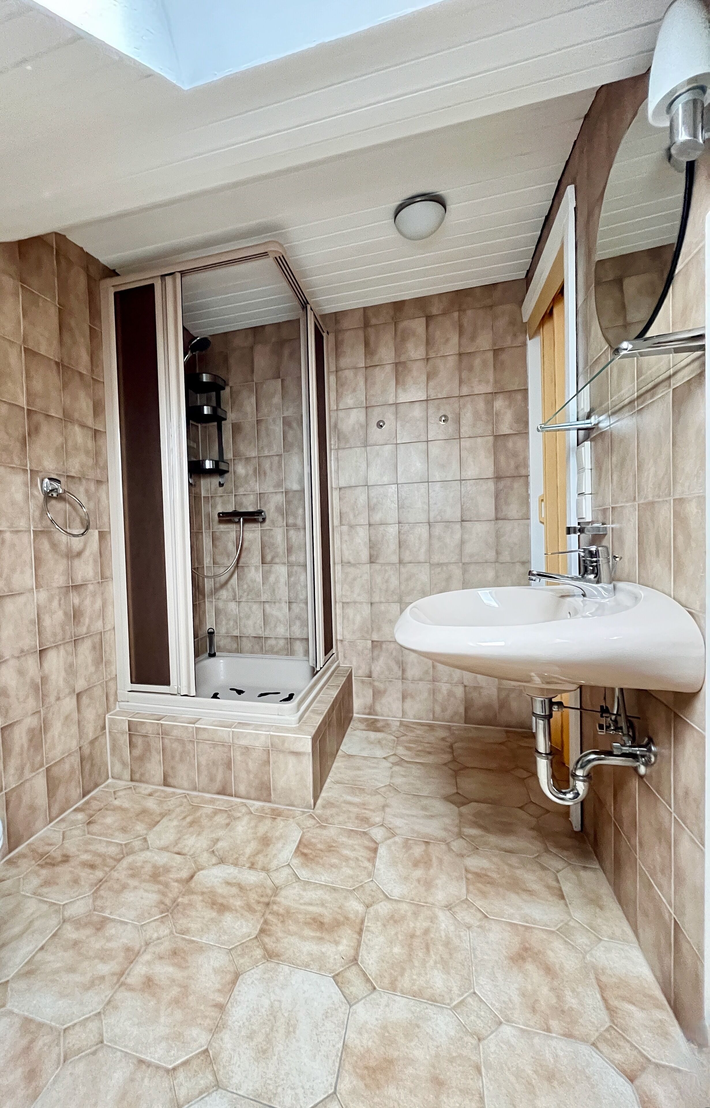 Un bagno moderno con piastrelle esagonali, una cabina doccia in vetro e un lavandino bianco.