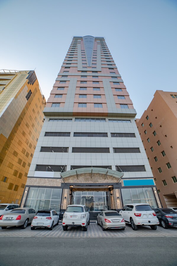 A tall hotel with a modern facade, multiple floors, and a parking lot with several cars.