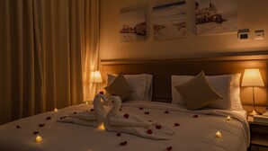 Une chambre d’hôtel avec un lit bien fait, deux horloges fixées au mur et une grande fenêtre avec des rideaux.