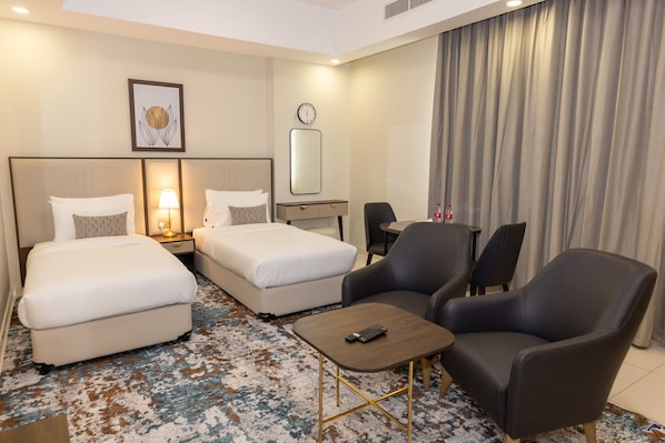 Une chambre d’hôtel avec deux lits, un bureau, une chaise, une petite table, une horloge et un tableau encadré au mur.