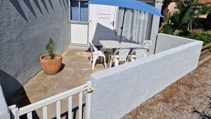 Pieni patio, jossa on pöytä ja tuolit, ruukussa oleva kasvi ja sininen aurinkovarjo.