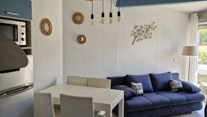 Moderni keittiö, jossa on mikroaaltouuni, ruokapöytä ja tuolit. Olohuoneessa on sininen sohva koristetyynyineen ja pieni sivupöytä.