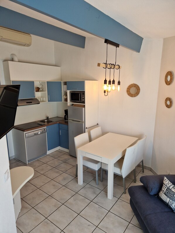A compact kitchen with a dining area, a sofa, and a ceiling light fixture.