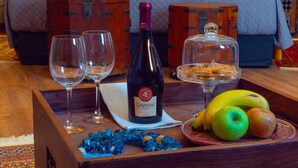 Een houten dienblad met een fles Granrosé wijn, twee lege wijnglazen, een bord met bananen en appels, en een glas water.
