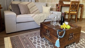 Een woonkamer met een grijze bank, een houten salontafel met fruit en glazen, een kamerkleed en een stenen muur.