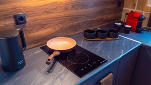 Een moderne keuken met een houten achterwand, een zwart inductiekookplaat, een pan en een koffiezetapparaat.