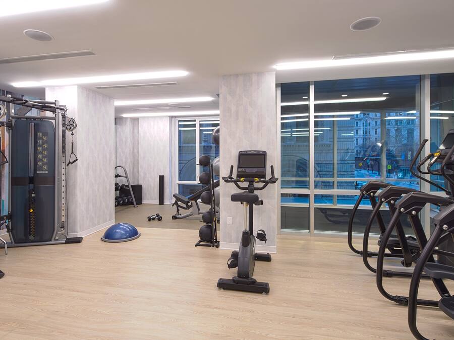 A modern gym with cardio machines, weightlifting equipment, and a large window offering a city view.