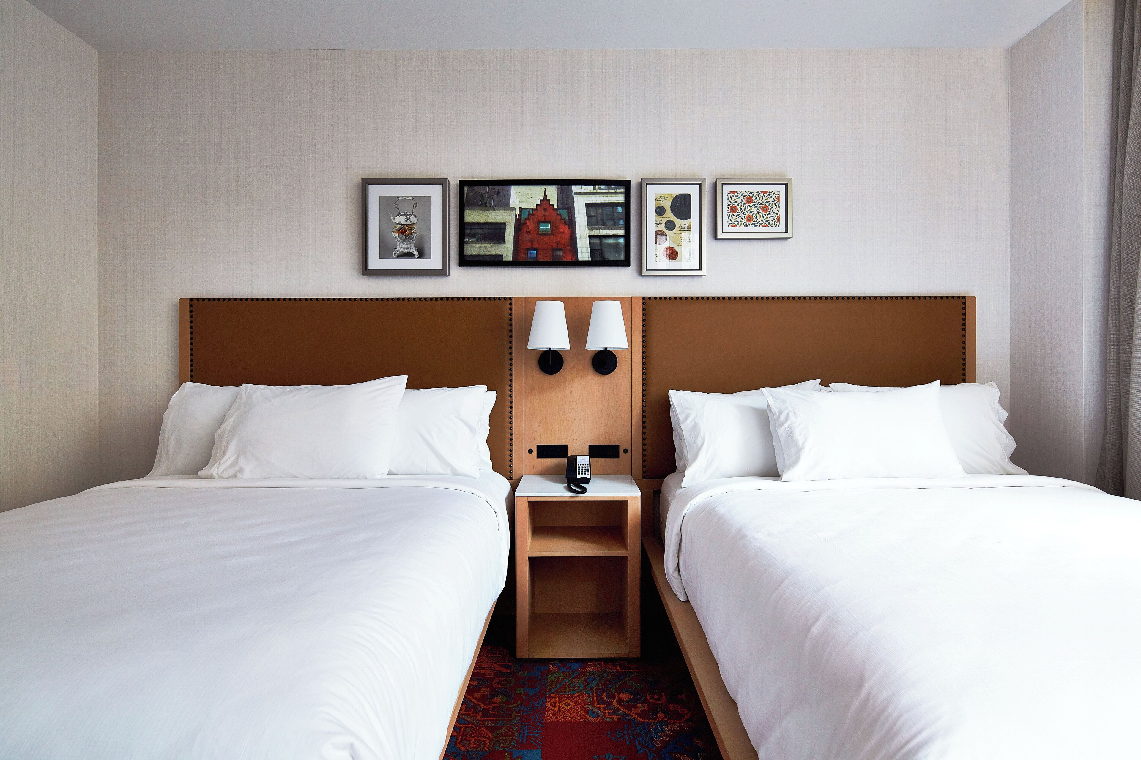 Ein Hotelzimmer mit zwei Betten, einem Nachttisch mit Lampe und einer Wand mit gerahmten Bildern.