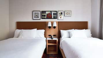 Habitación de hotel con dos camas, una mesita de noche con lámpara y una pared decorada con cuadros.