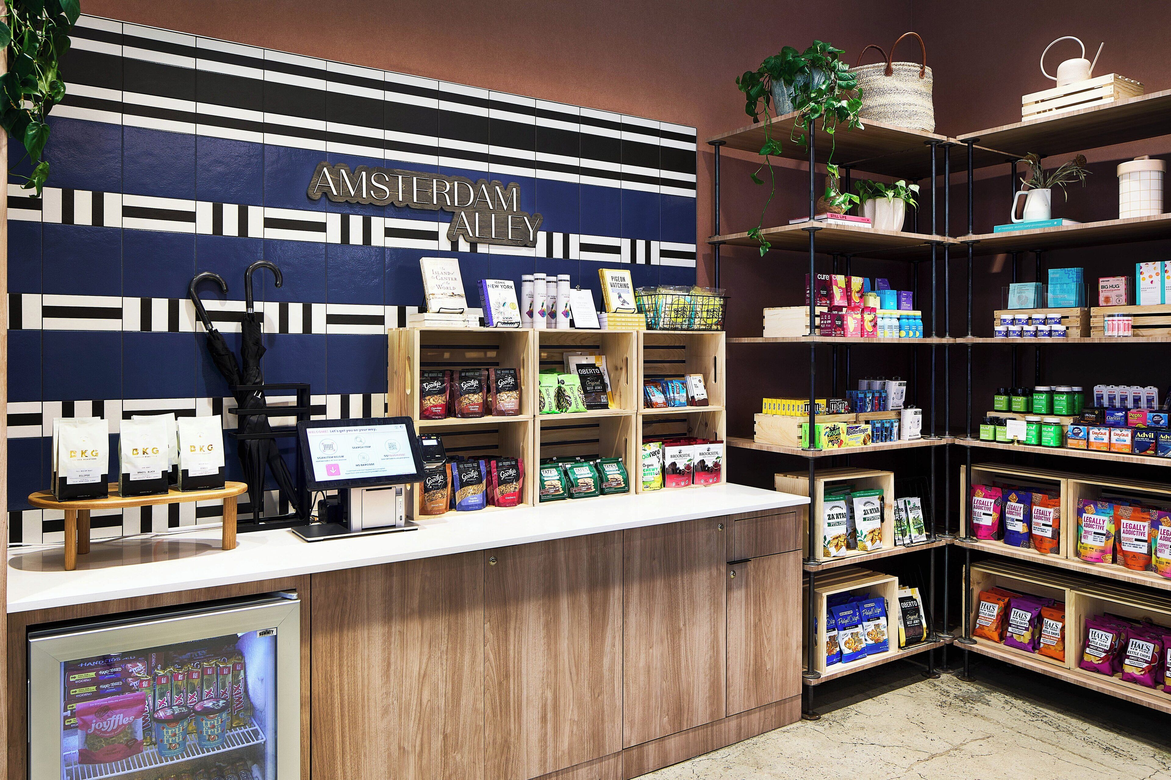 A store interior with a counter displaying various products, shelves stocked with snacks, and a sign reading "AMSTERDAM ALLEY".