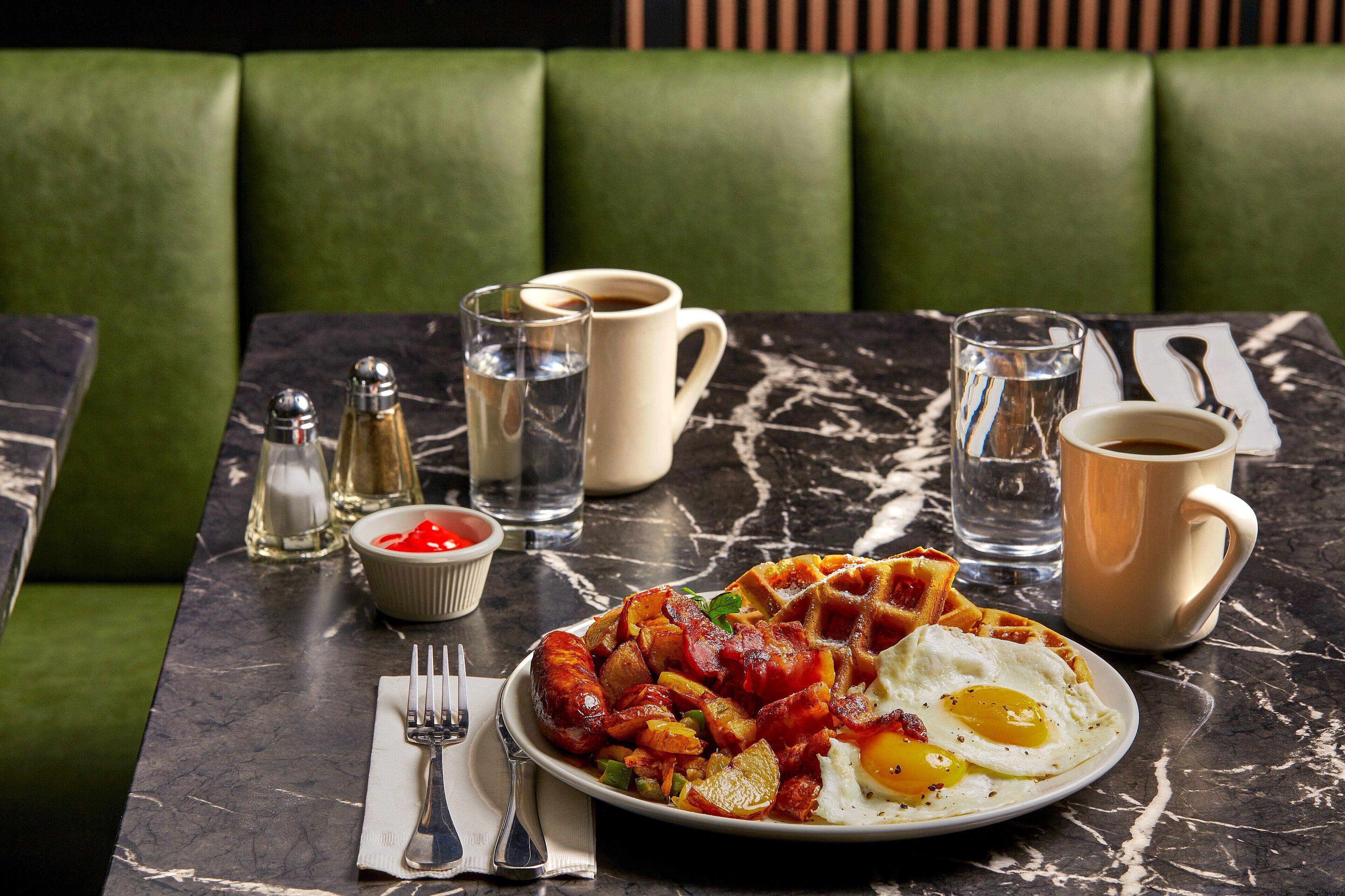 A breakfast plate with sausage, potatoes, and a fried egg, accompanied by coffee and condiments on a marble table.