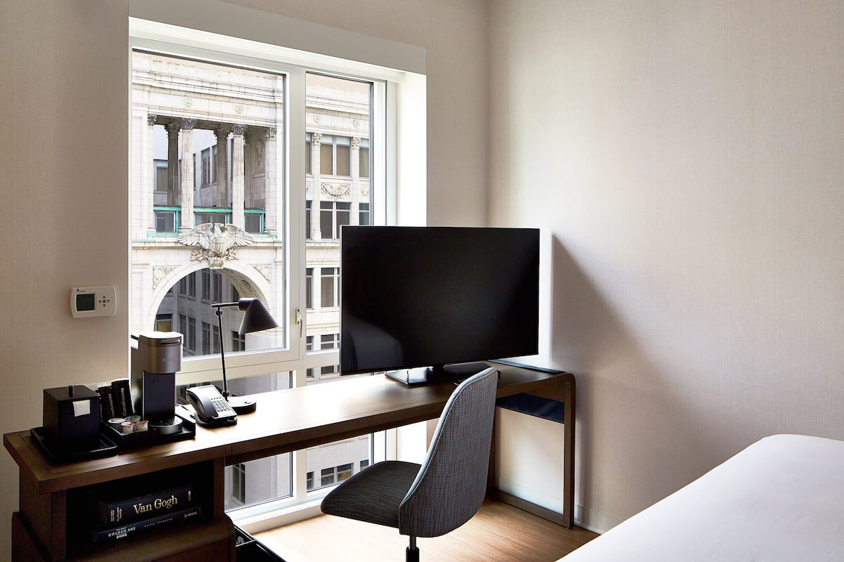 Une chambre d’hôtel dotée d’une grande fenêtre, d’un bureau avec un téléviseur à écran plat, d’une chaise et d’un lit.