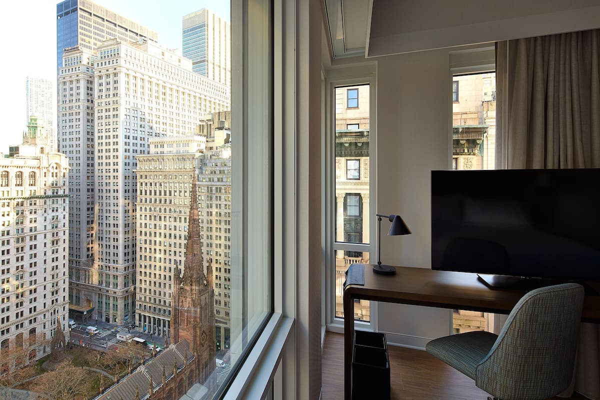 Une chambre d’hôtel dotée d’une grande fenêtre donnant sur la ville, d’un téléviseur à écran plat et d’un bureau avec une chaise.