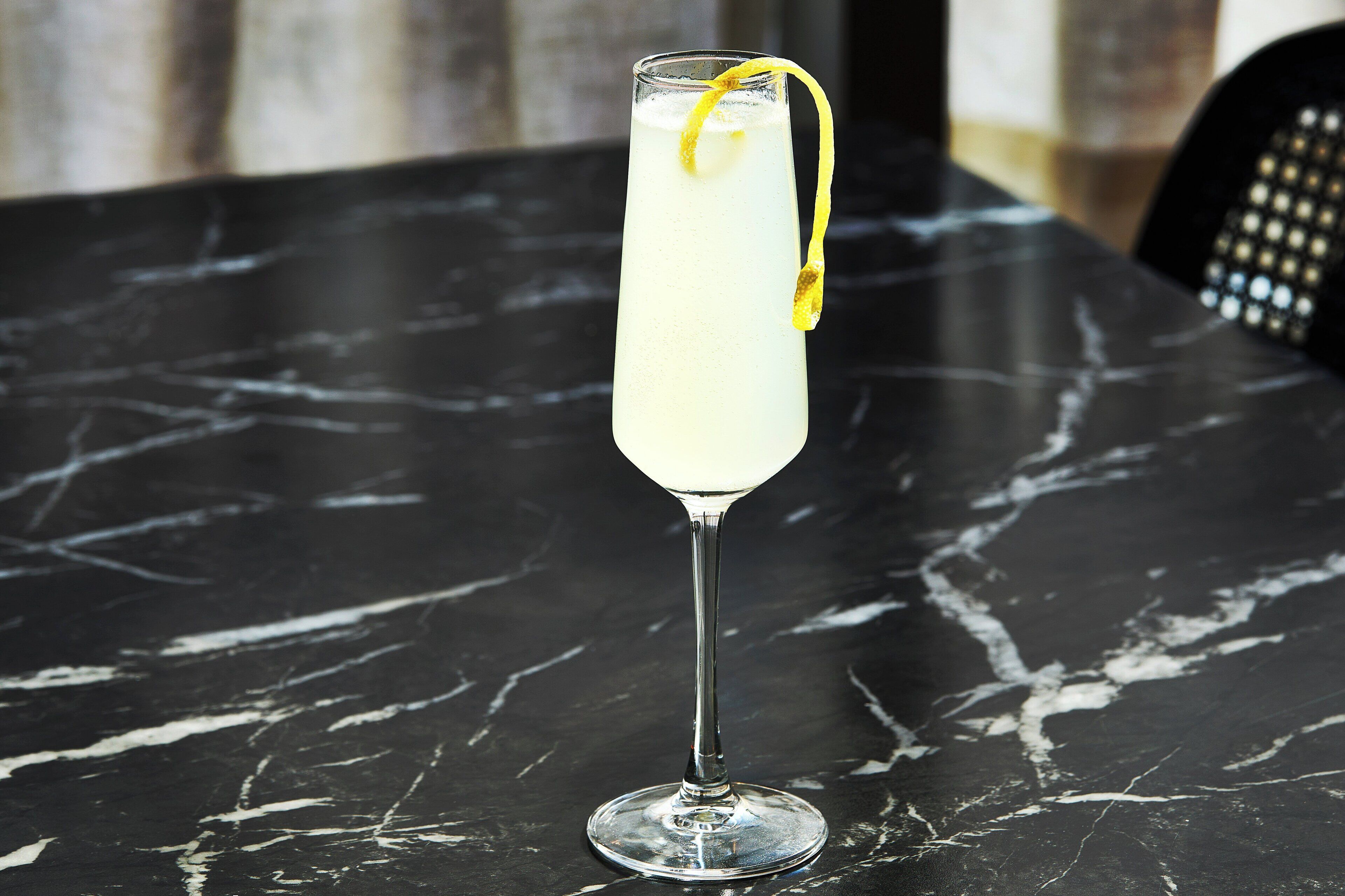 A tall glass with a lemon twist on a marble table.