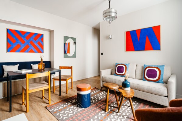 A modern living room with a sofa, chairs, a dining table, and artwork on the walls.