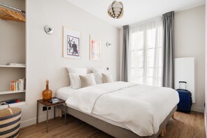 Une chambre d’hôtel avec un grand lit, une table de chevet, une lampe, une fenêtre avec des rideaux et une bibliothèque.
