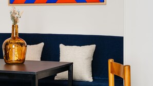 Ein Zimmer mit einem dunkelblauen Sofa, einem Holzstuhl, einem kleinen Tisch und einem farbenfrohen, abstrakten Gemälde an der Wand.