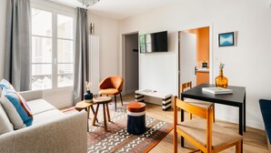 Ein modernes Wohnzimmer mit einer Couch, einem Esstisch, einem an der Wand montierten Fernseher und Blick auf den Balkon.