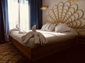 A neatly made bed with white linens and decorative pillows, a wall-mounted light fixture, and a decorative wall panel.