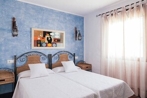 Une chambre avec deux lits, un mur bleu à texture, un tableau et une fenêtre avec des rideaux légers.