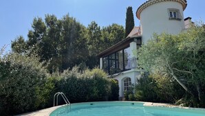 En swimmingpool omgivet af frodig vegetation og en hvid bygning med balkon.