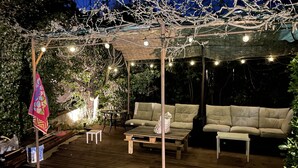 En udendørs terrasse med træterrasse, to beige sofaer, et lille rundt bord og lyskæder.