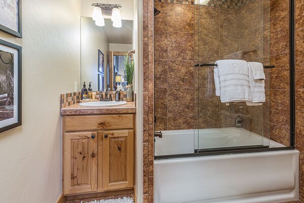 Un baño con tocador de madera, ducha con cerramiento de vidrio y bañera blanca.