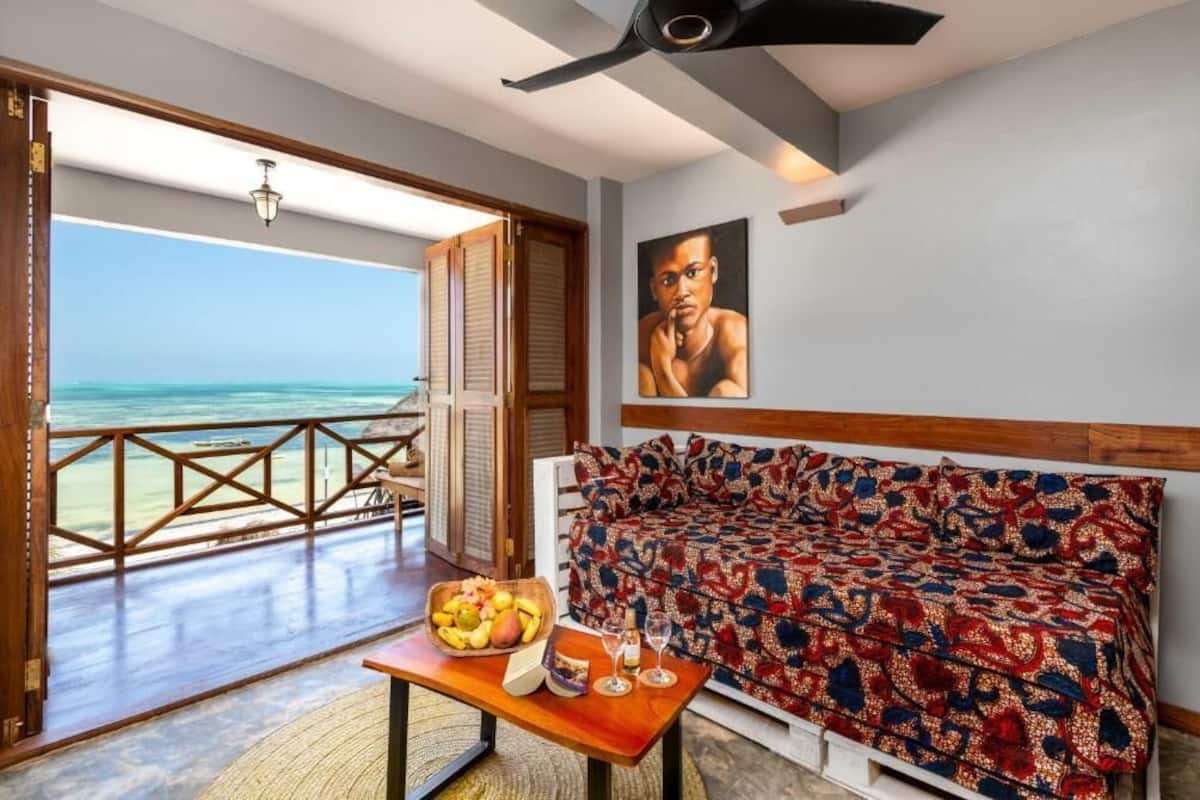 Una habitación con vista al océano, una mesa de madera con fruta y vasos, y un sofá estampado.