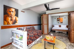A compact room with a bed, a sofa, a small table with fruits, and a bookshelf. - Pili Pili Nautica (Jambiani)