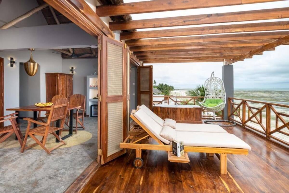 Una terraza de madera con una silla de descanso, una mesa de comedor con sillas y vista al mar.