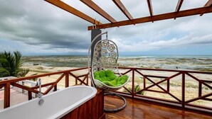 Una terraza de madera con una silla colgante y una bañera con vistas a la playa.