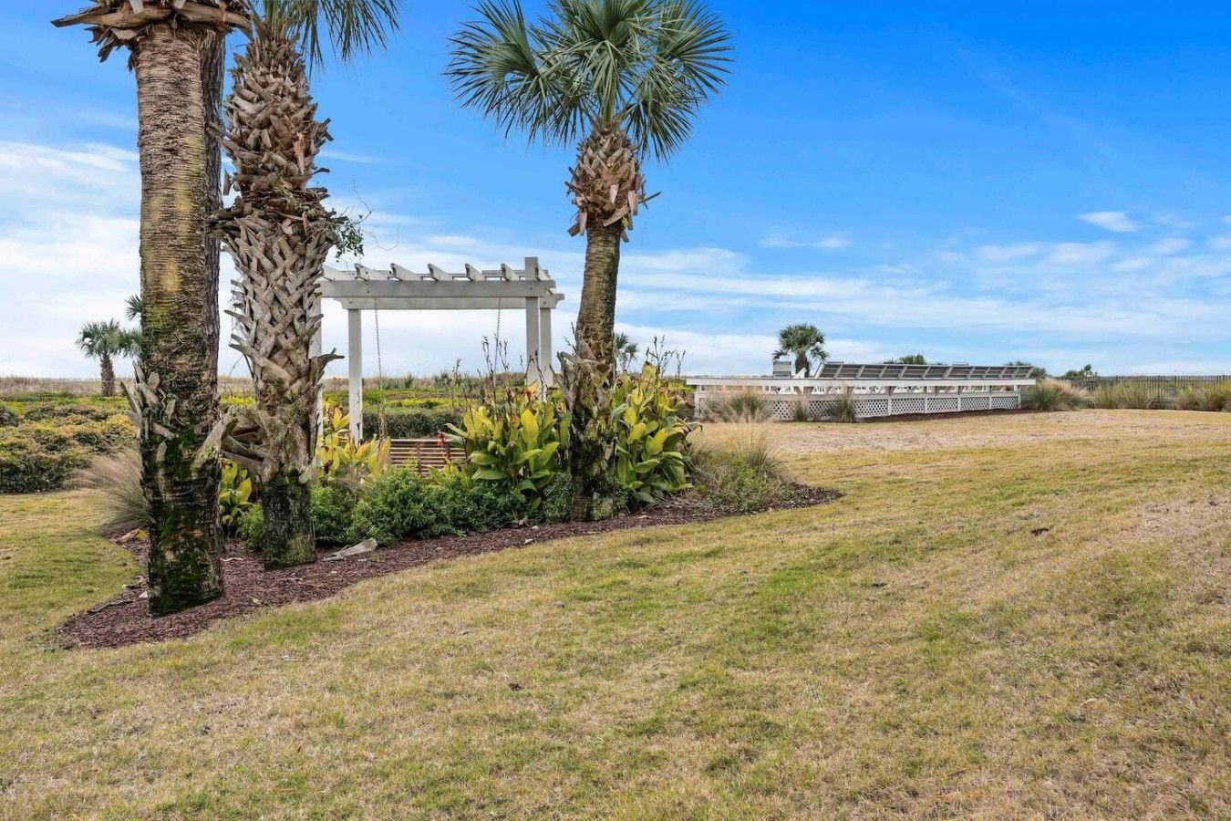 Un jardín con palmeras, una pérgola y una valla.