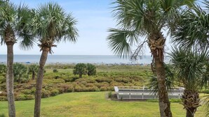 A view of a beach with palm trees and a white fence in the foreground. - Oceanfront Sunrises in Upgraded Seaside Villa 225 (Hilton Head Island)