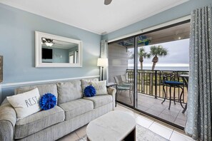 A living room with a sofa, a coffee table, a balcony with a table and chairs, and a view of the ocean. - Oceanfront Sunrises in Upgraded Seaside Villa 225 (Hilton Head Island)