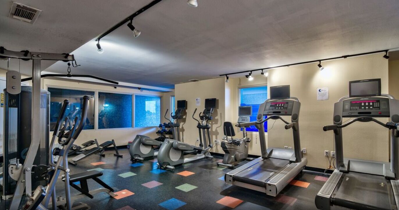 A gym with various exercise machines, a large window, and a wall-mounted TV.