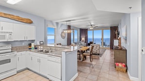 Une cuisine spacieuse dotée d’un îlot central, un coin repas offrant une vue dégagée et un salon avec un balcon donnant sur la mer.