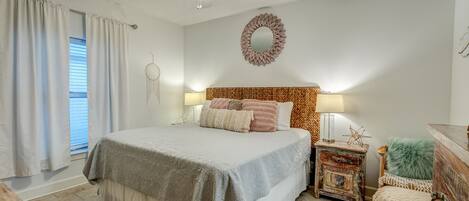 A bedroom with a bed, bedside lamps, a decorative wall mirror, a ceiling fan, and a window with curtains.