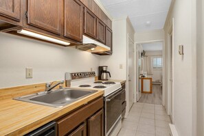A compact kitchen with wooden cabinets, a stainless steel sink, a stove, and a coffee maker. - 1 bedroom, oceanfront condo, north OC, beautiful views!! (Ocean City)